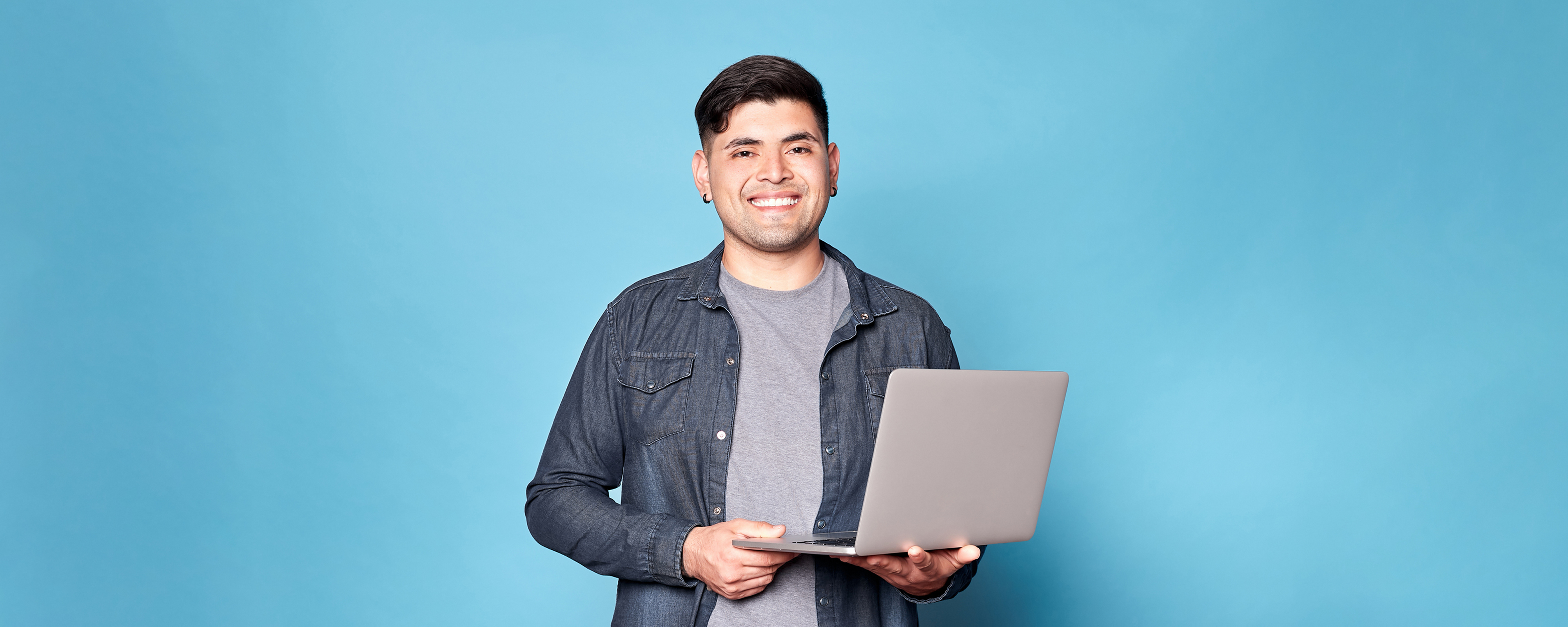 Image of a person standing, holding a laptop and smiling at the camera